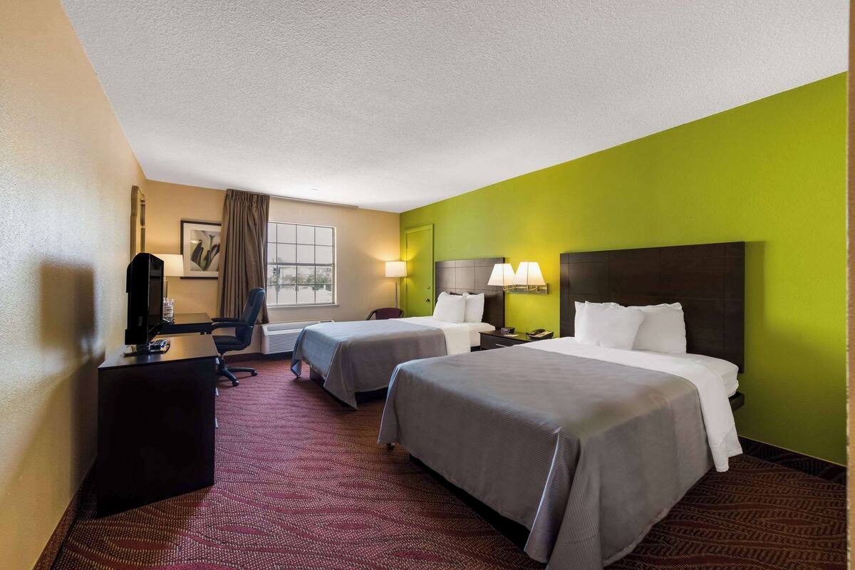 A hotel room with two beds, a desk, a chair, and a television.