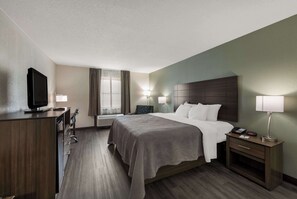 A hotel room with a bed, bedside table, lamp, TV, and a desk with a chair. - Quality Inn Saint Louis Airport (St. Louis)