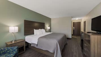 A hotel room with a bed, bedside table, lamp, TV, and a small seating area.