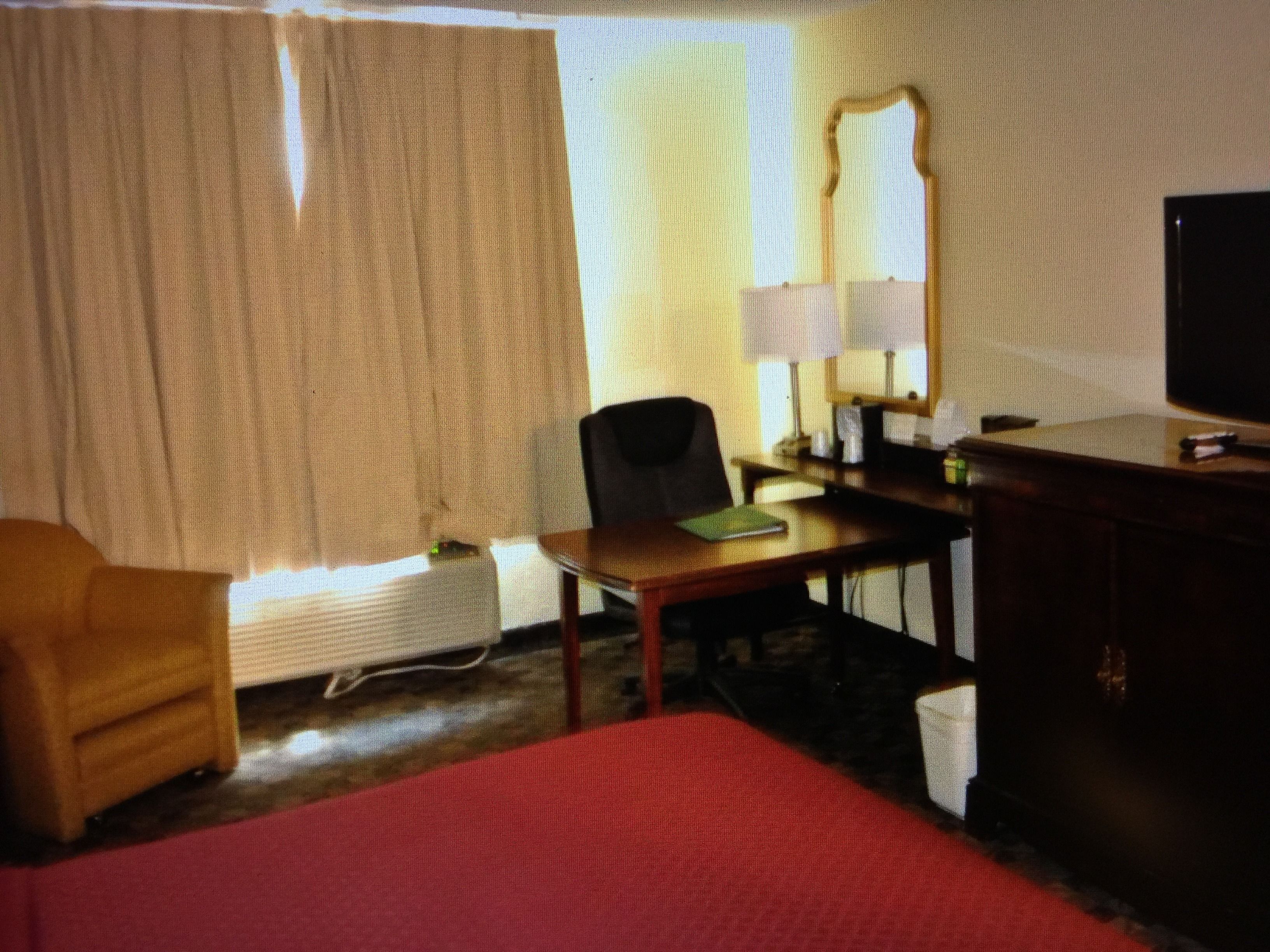 A hotel room with a bed, a desk, a chair, a television, and a window with curtains.
