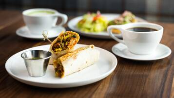 Una mesa con un burrito, una taza de café y un plato de ensalada.