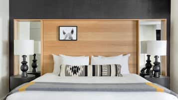 A hotel room with a wooden headboard, two bedside tables with lamps, a bed with white and patterned pillows, and a framed picture on the headboard.
