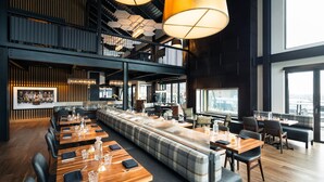 Un restaurante moderno con una larga mesa común, asientos individuales y grandes ventanales con vistas.