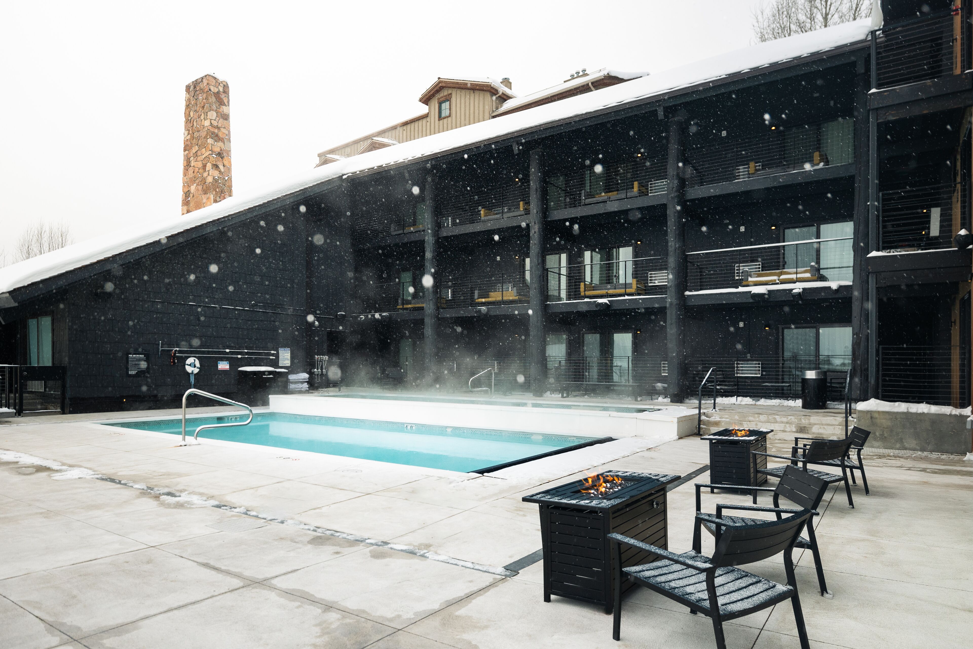A pool area with a stone chimney, outdoor seating, and a building with multiple balconies.