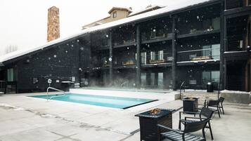A pool area with a stone chimney, outdoor seating, and a building with multiple balconies.