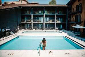 En swimmingpool med en person i badkläder vid kanten, en livräddarstol och en solstol.