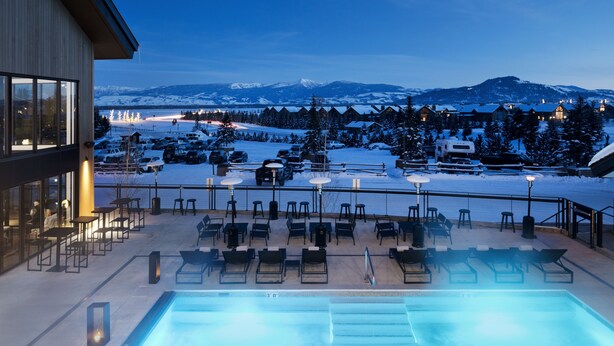 Zona de piscina con sillones de descanso y vistas a montañas nevadas.