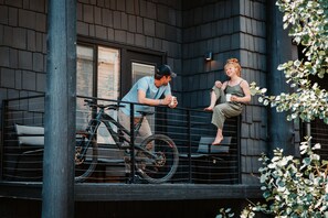 A balcony with a bicycle, a person leaning on the railing, and another person sitting on the edge. - Gravity Haus Jackson Hole (Teton Village)