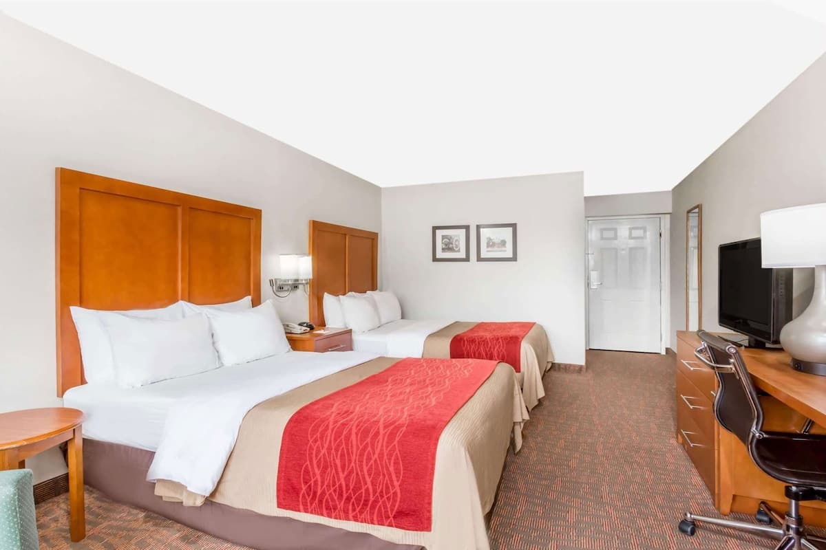 A hotel room with two beds, a desk with a chair, a television, and a door.