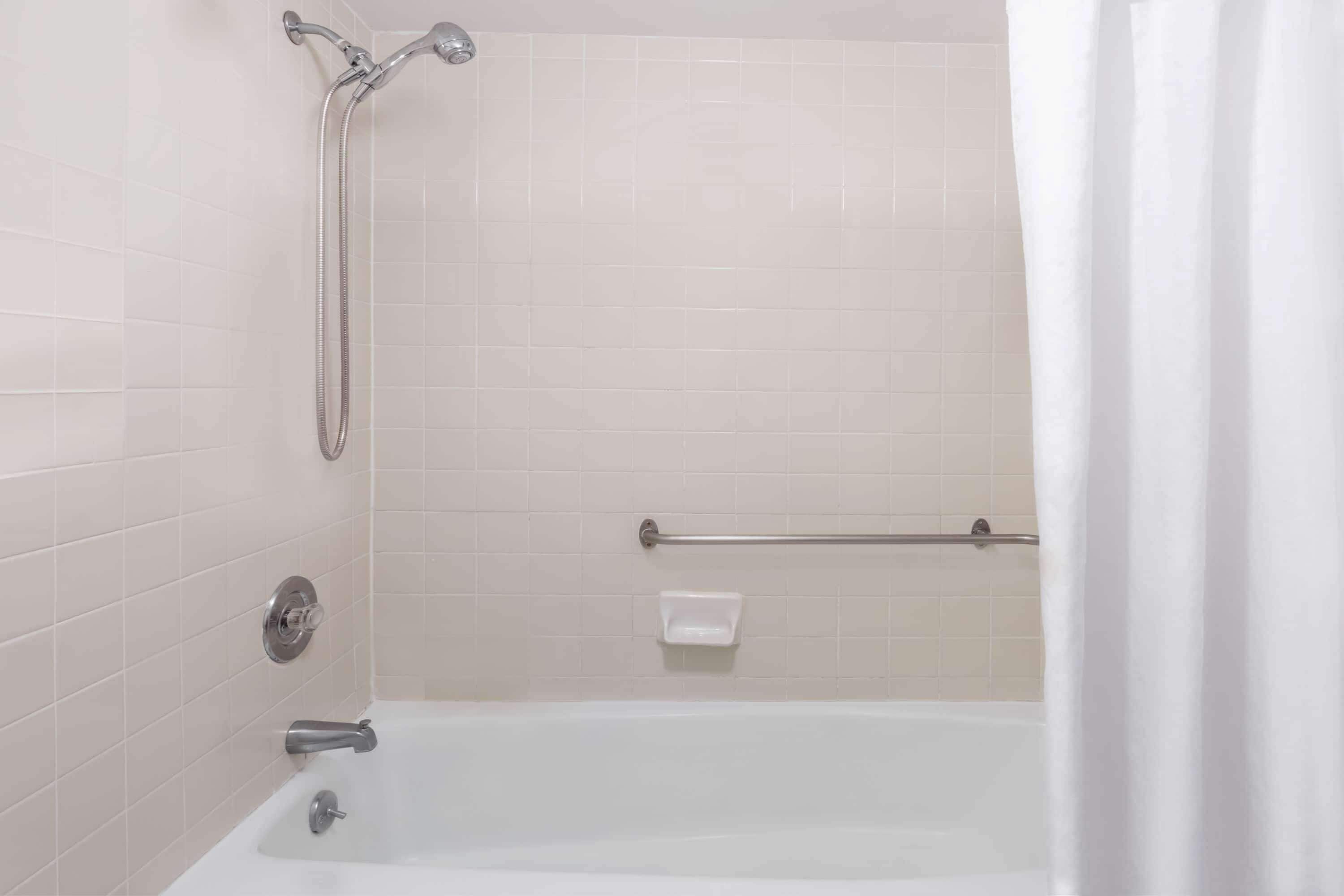 A bathroom with a bathtub, a shower, and a handrail.