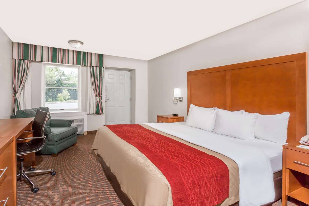 A hotel room with a large bed, a desk, a chair, and a window with curtains.