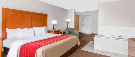 Habitación de hotel con una cama grande, un escritorio, una silla, una lámpara, una puerta y una bañera.