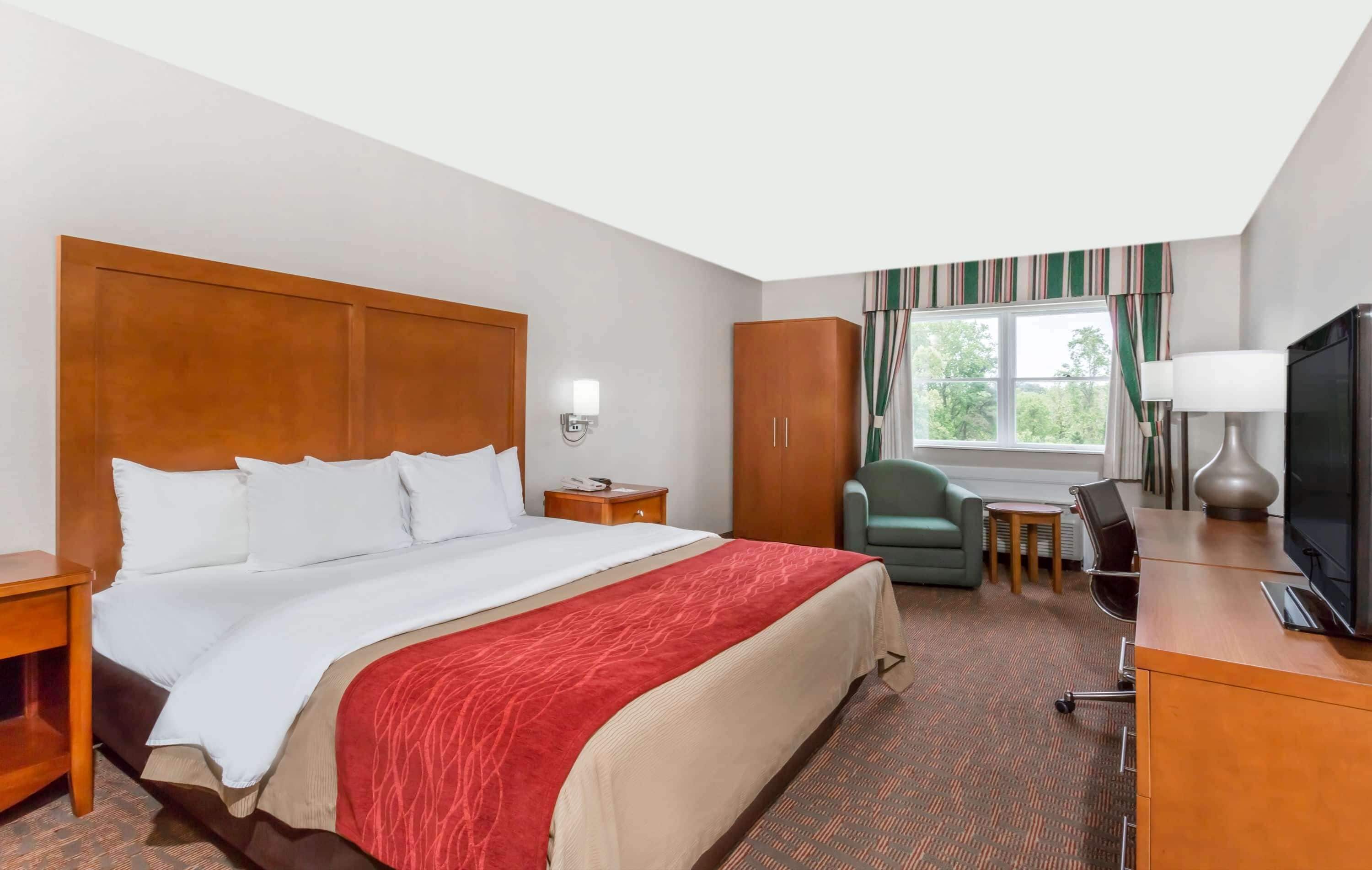 A hotel room with a large bed, a desk with a chair, a television, and a wardrobe.