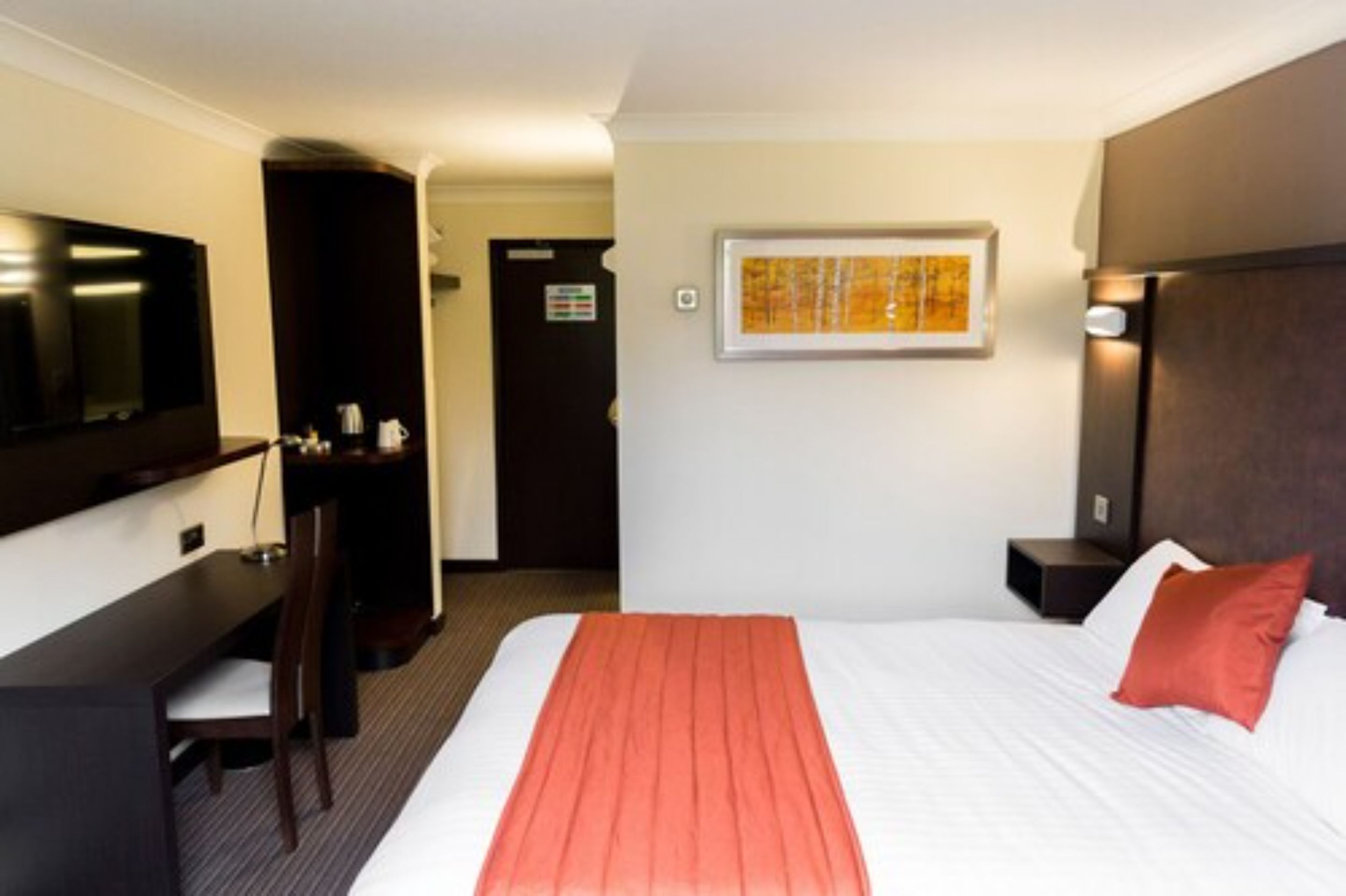 A hotel room with a bed, a desk, a chair, a television, and a framed picture on the wall.