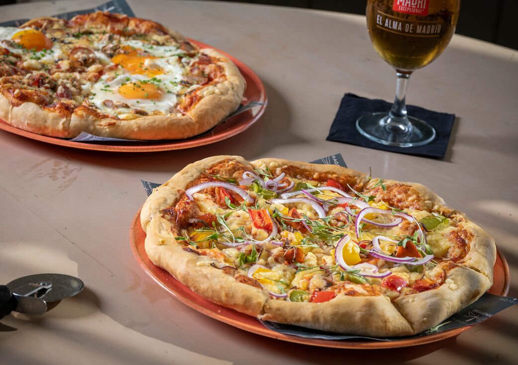 Two pizzas on plates with a wine glass on a table.