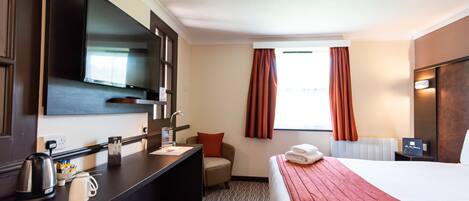 A hotel room with a bed, a desk, a chair, a television, and a window with curtains.