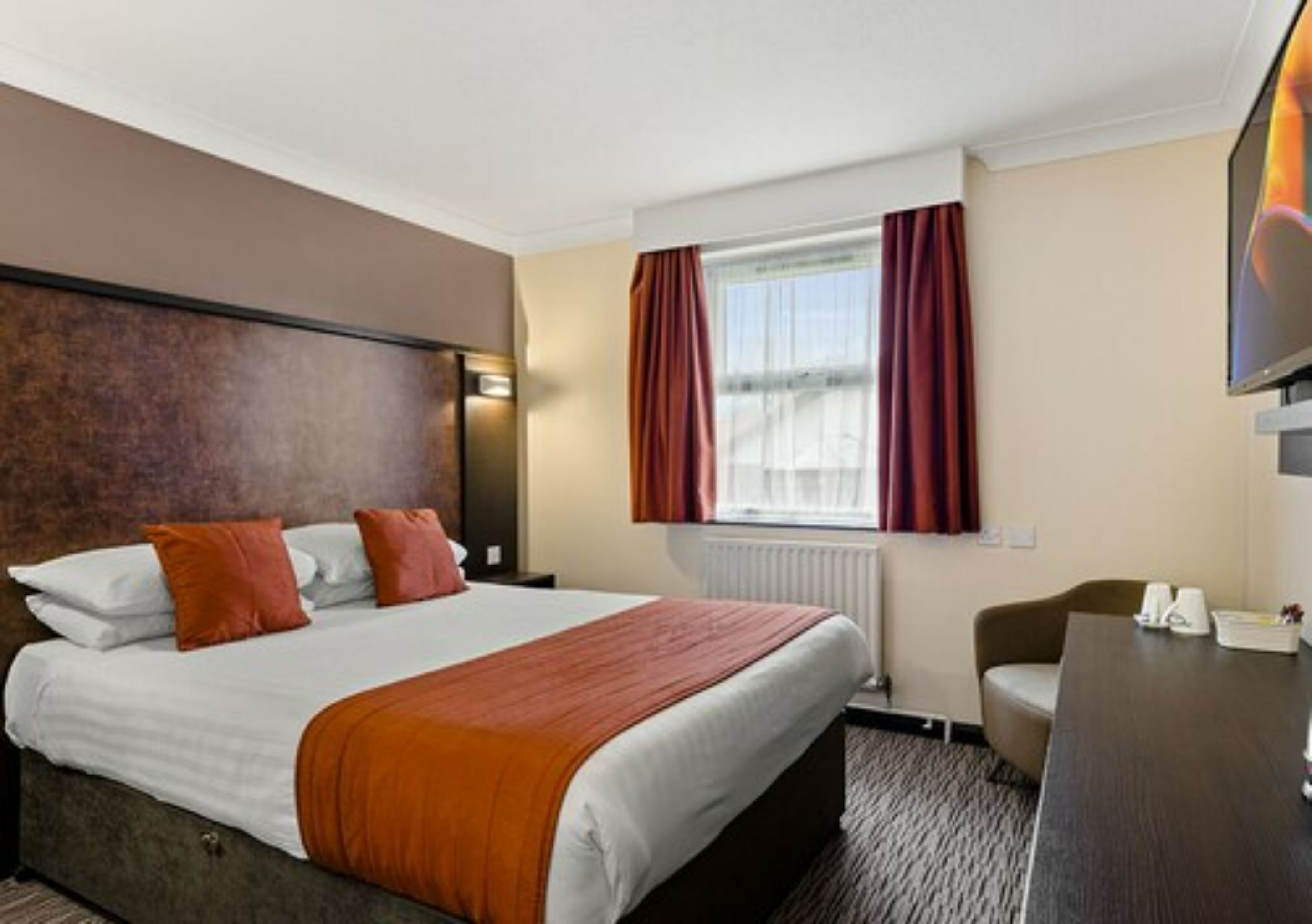 A hotel room with a bed, a desk, a chair, a TV, and a window with curtains.