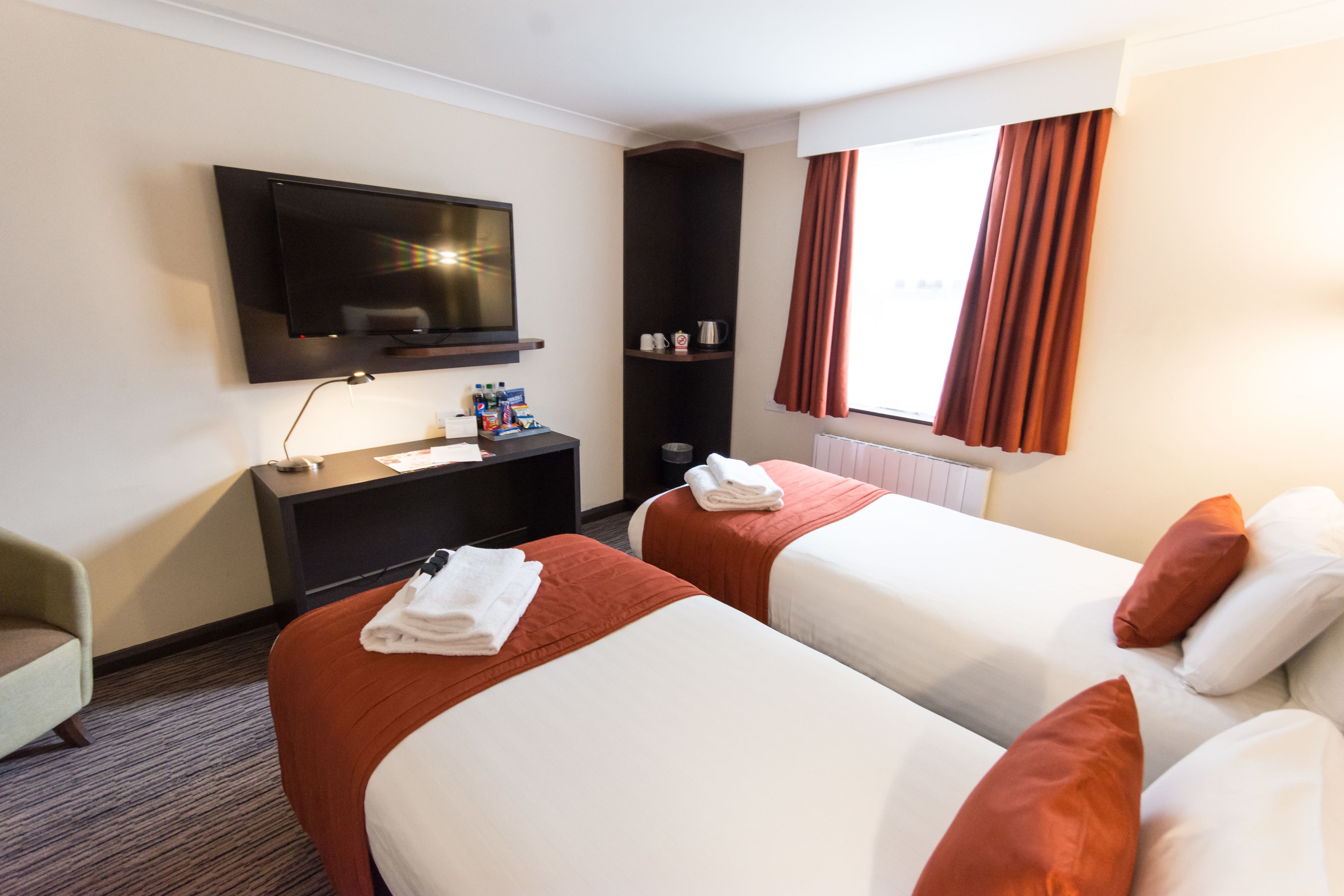 Habitación de hotel con dos camas, televisor, escritorio y ventana con cortinas.