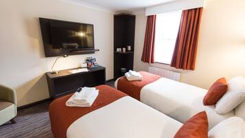 A hotel room with two beds, a TV, a desk, and a window with curtains.
