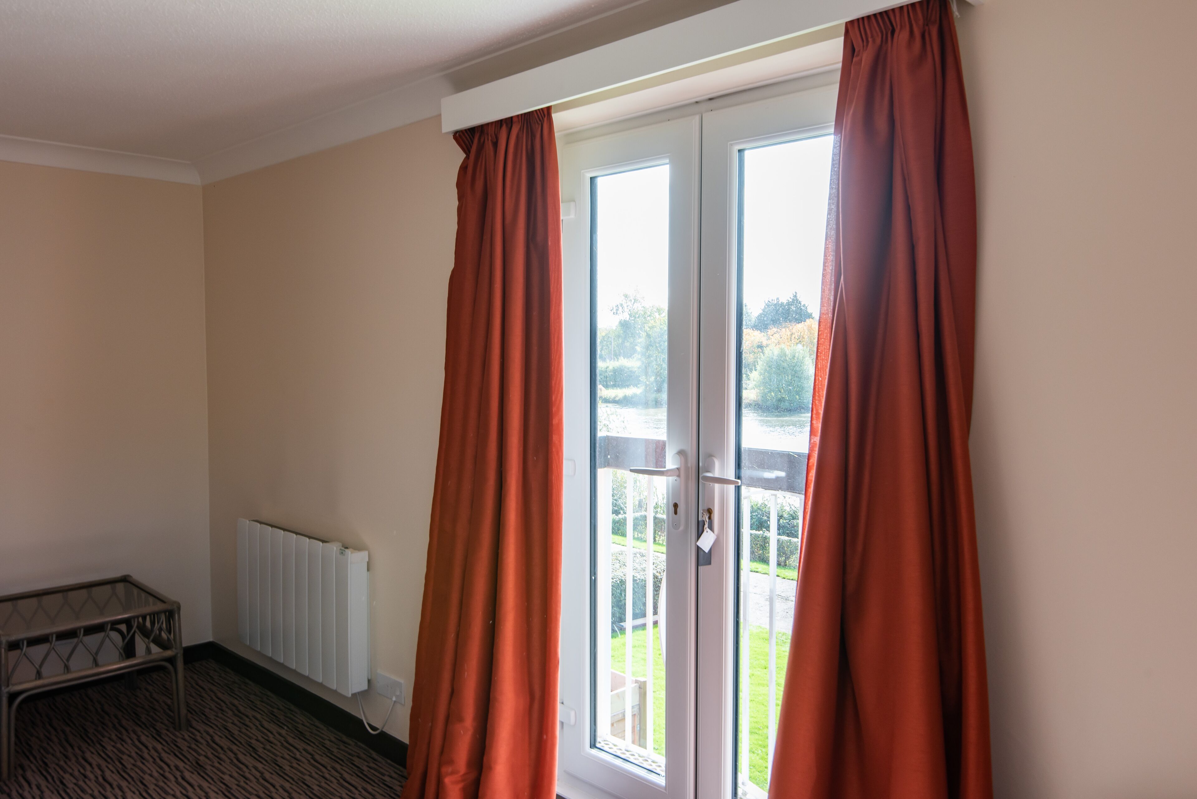 A room with a radiator, a small table, and a view through a glass door with curtains.