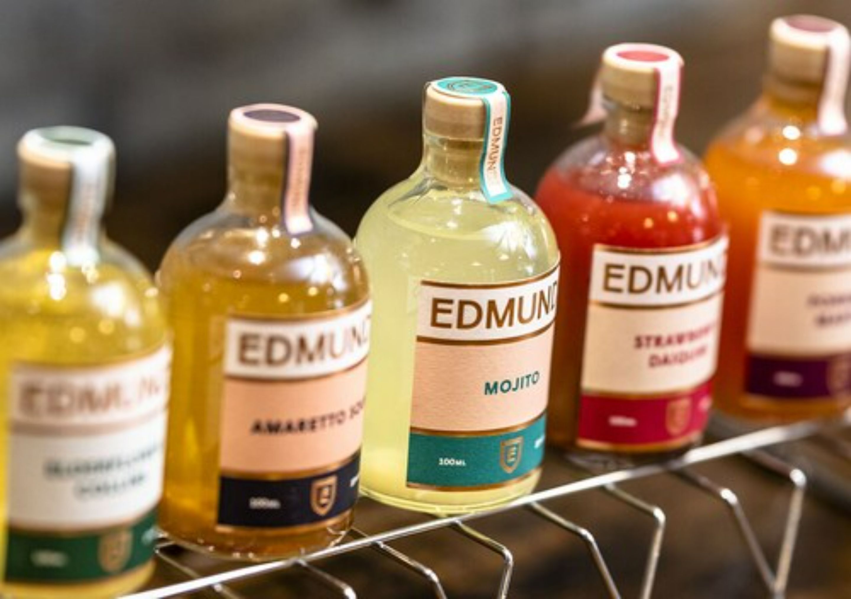 Una estantería con varias botellas de licor de la marca Edmun, incluyendo Mojito y Strawberry Daiquiri.