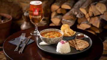 A dining table with a bowl of soup, rice, flatbread, a glass of beer, and a small bowl of sauce.