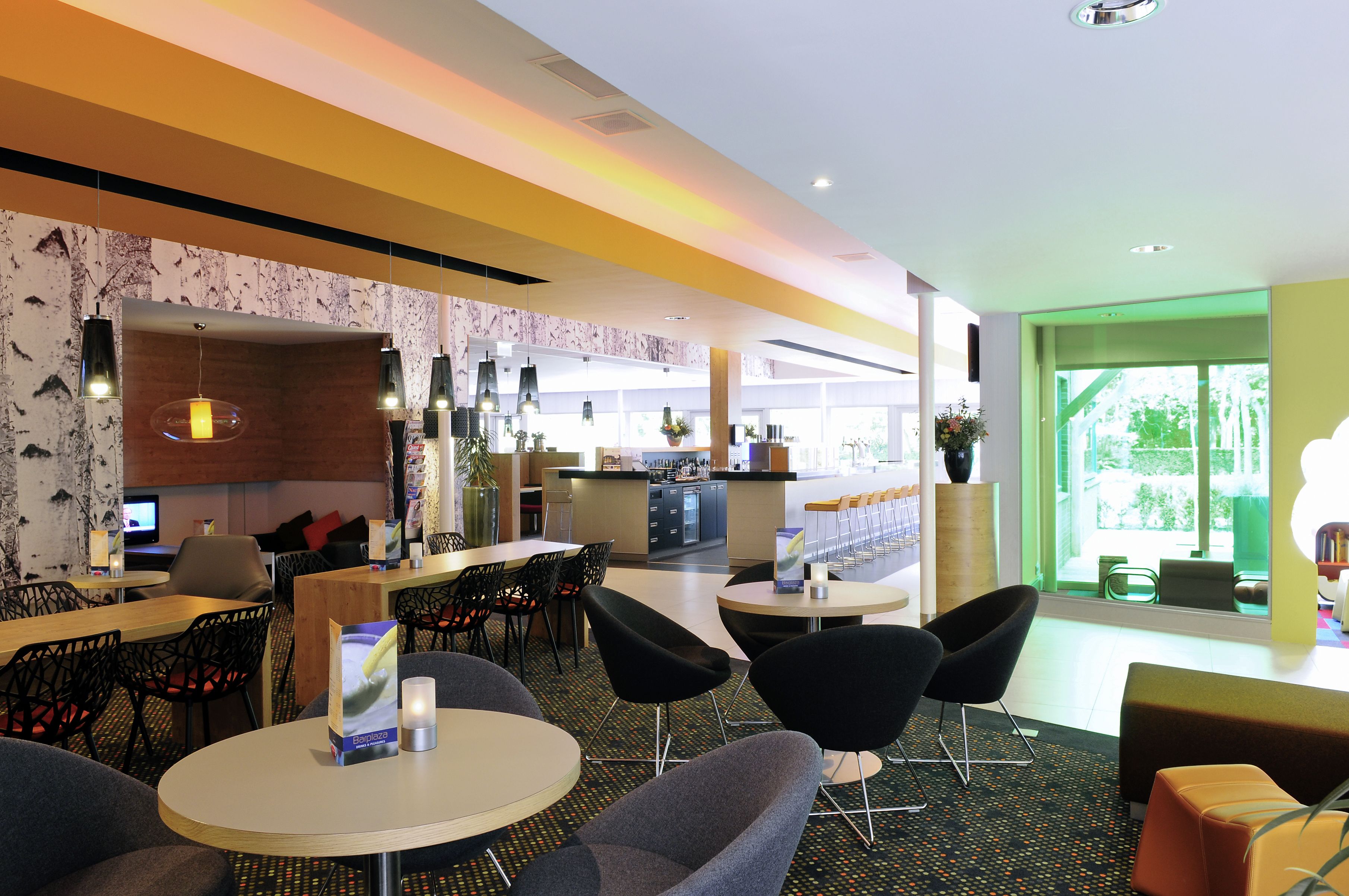 Eine moderne Hotelhalle mit runden Tischen, schwarzen Stühlen, einer Bar und großen Fenstern mit Blick ins Freie.