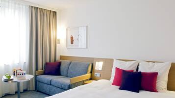 A hotel room with a bed, a sofa, a small table with a plate of apples, and a window with curtains.
