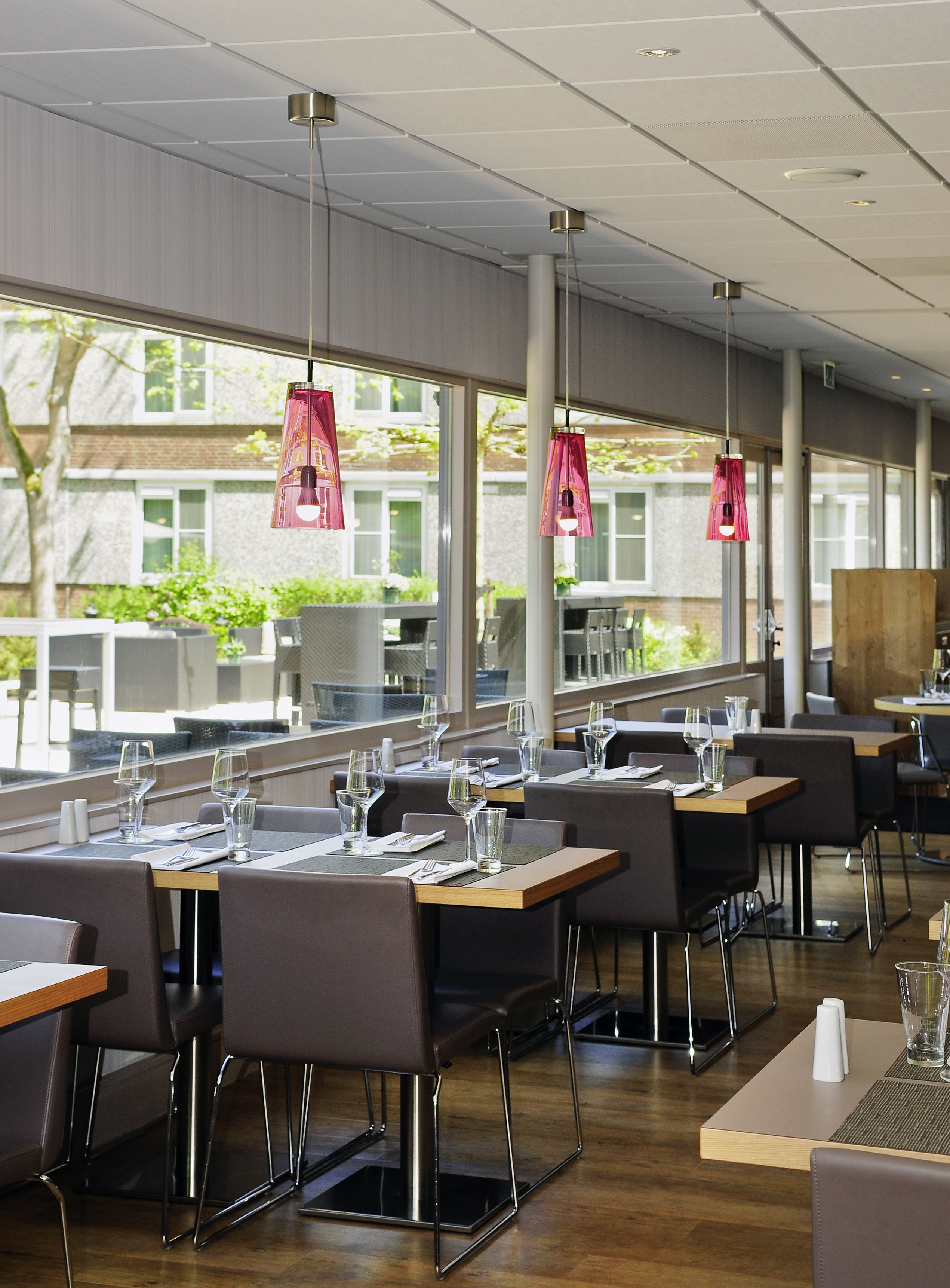A modern restaurant with large windows, wooden tables, and black chairs.