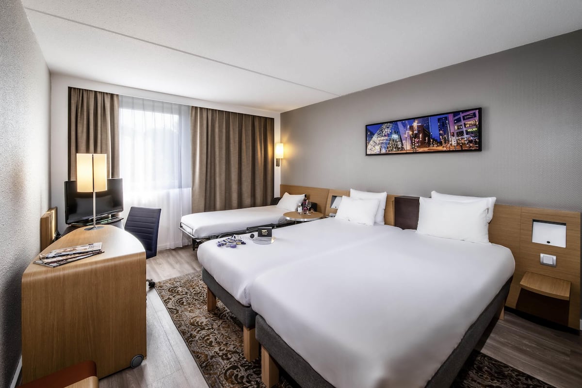 A hotel room with a large bed, a desk, a chair, a TV, and a painting on the wall.
