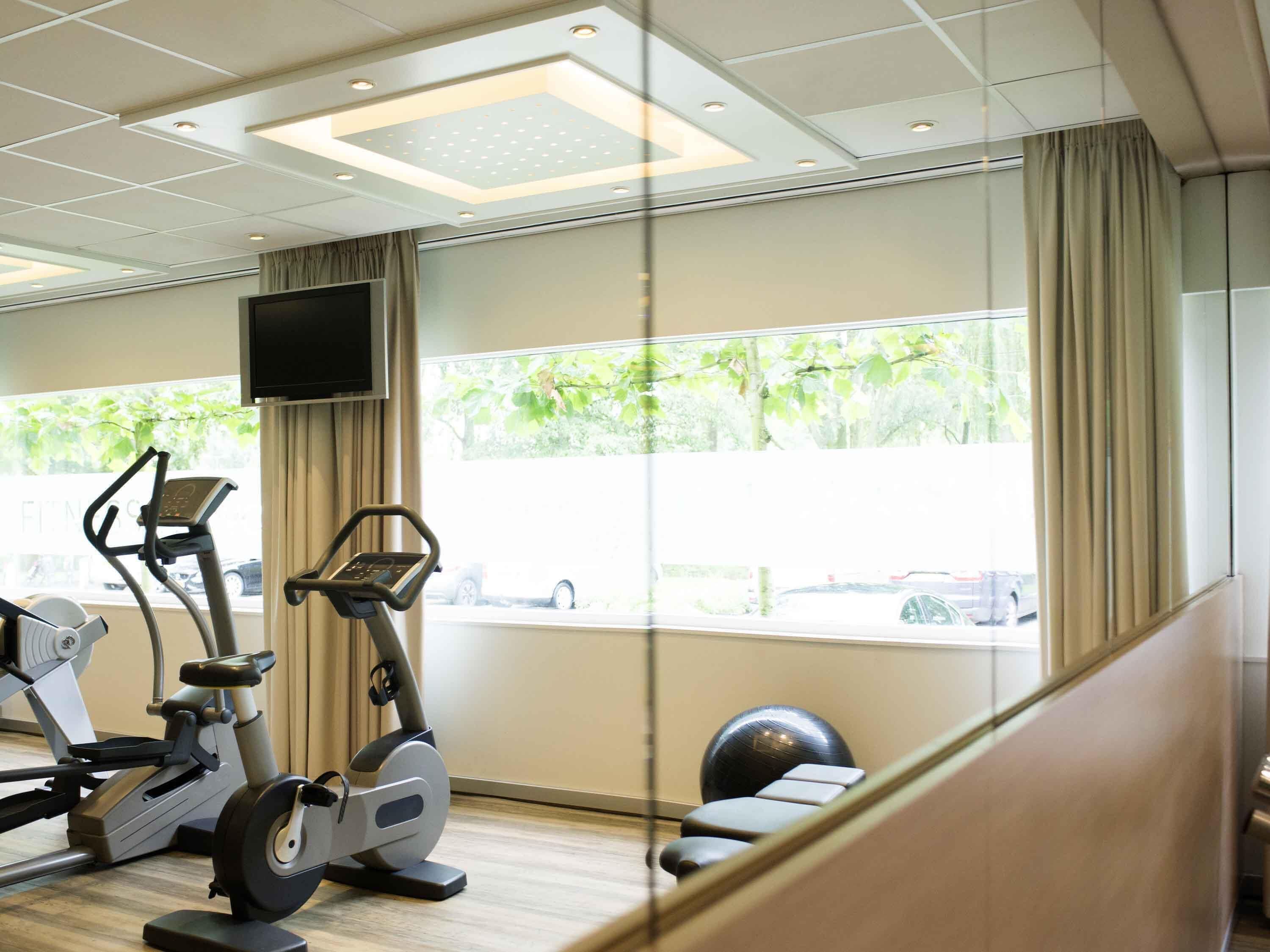 Un gimnasio con equipo de ejercicio, un televisor y amplias ventanas con vistas a zonas verdes.