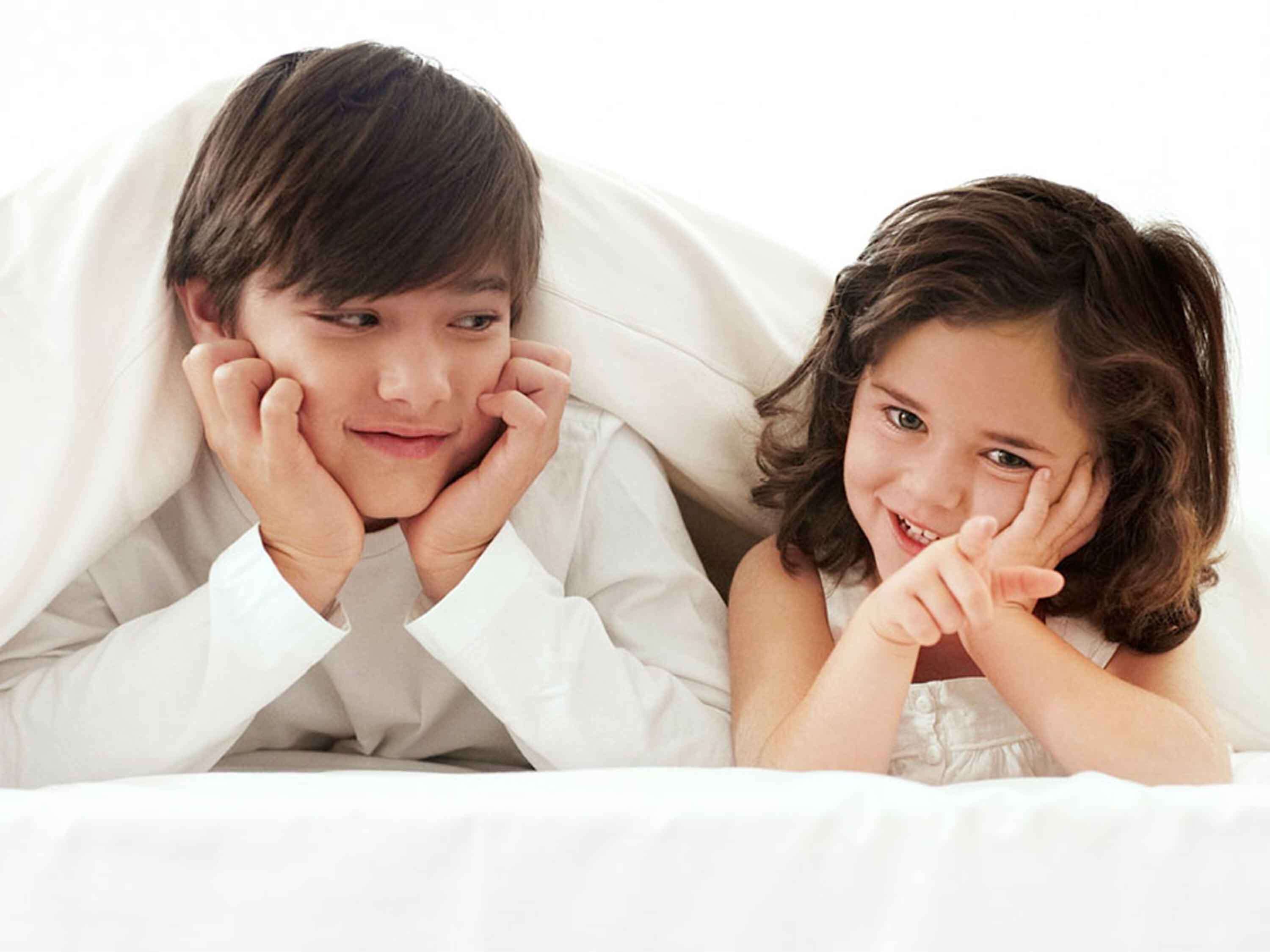 Een kind en volwassene liggen in bed, onder een witte deken.