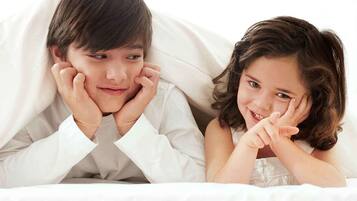 A child and an adult lying in bed, covered with a white blanket.