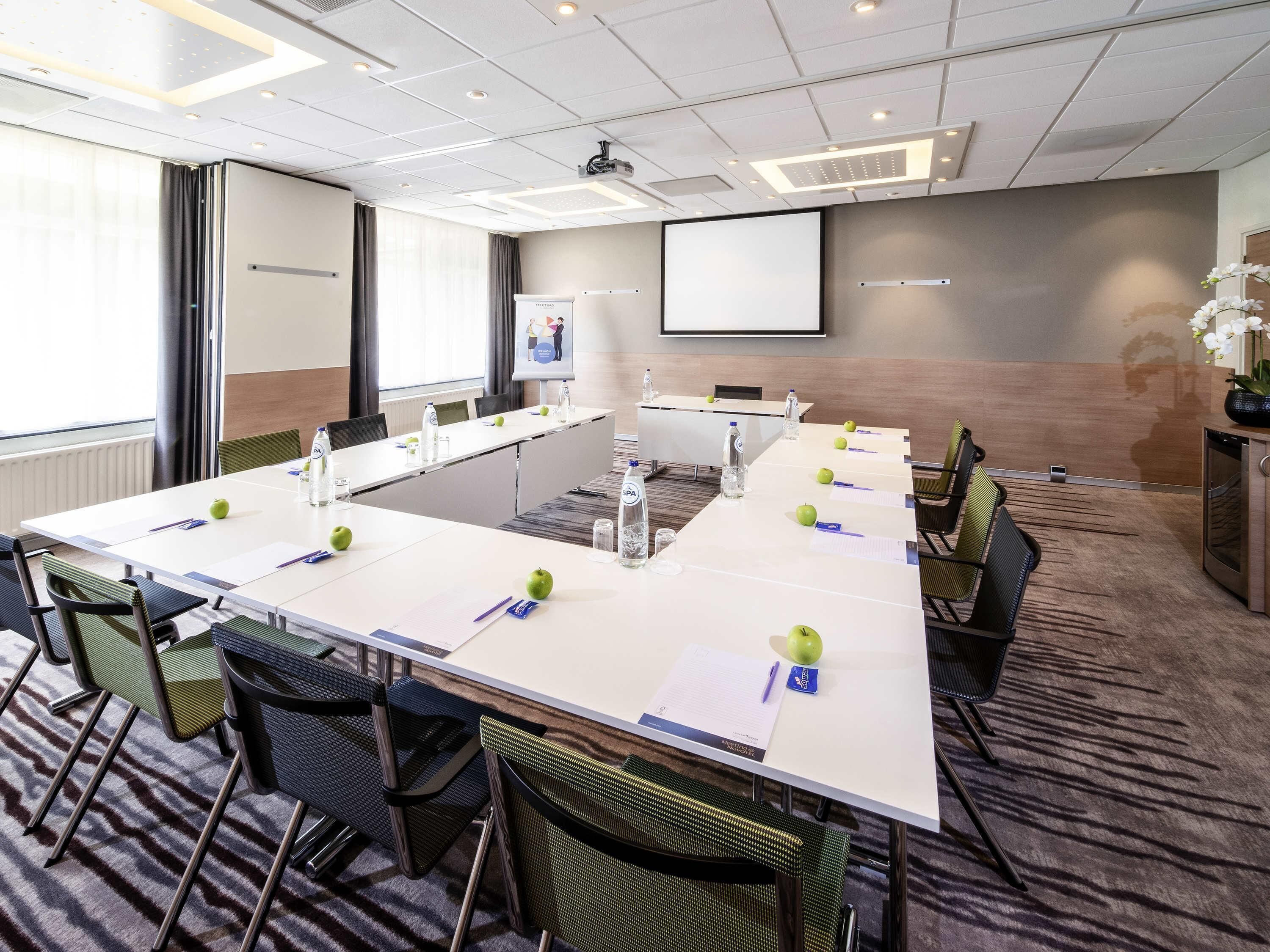 A conference room with a long table, chairs, a projector screen, and a whiteboard.