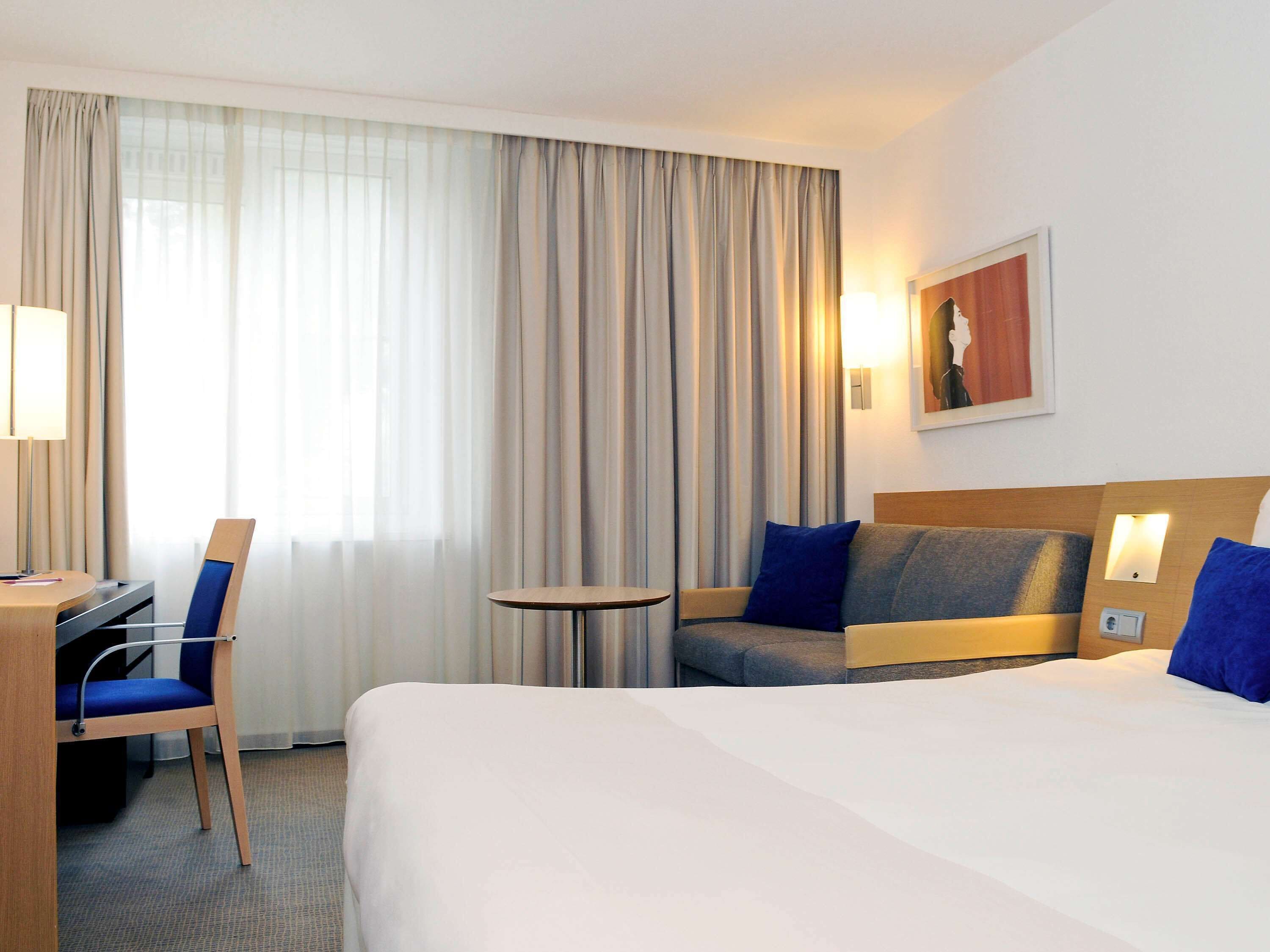 A hotel room with a bed, a desk, a chair, a small table, and a sofa.