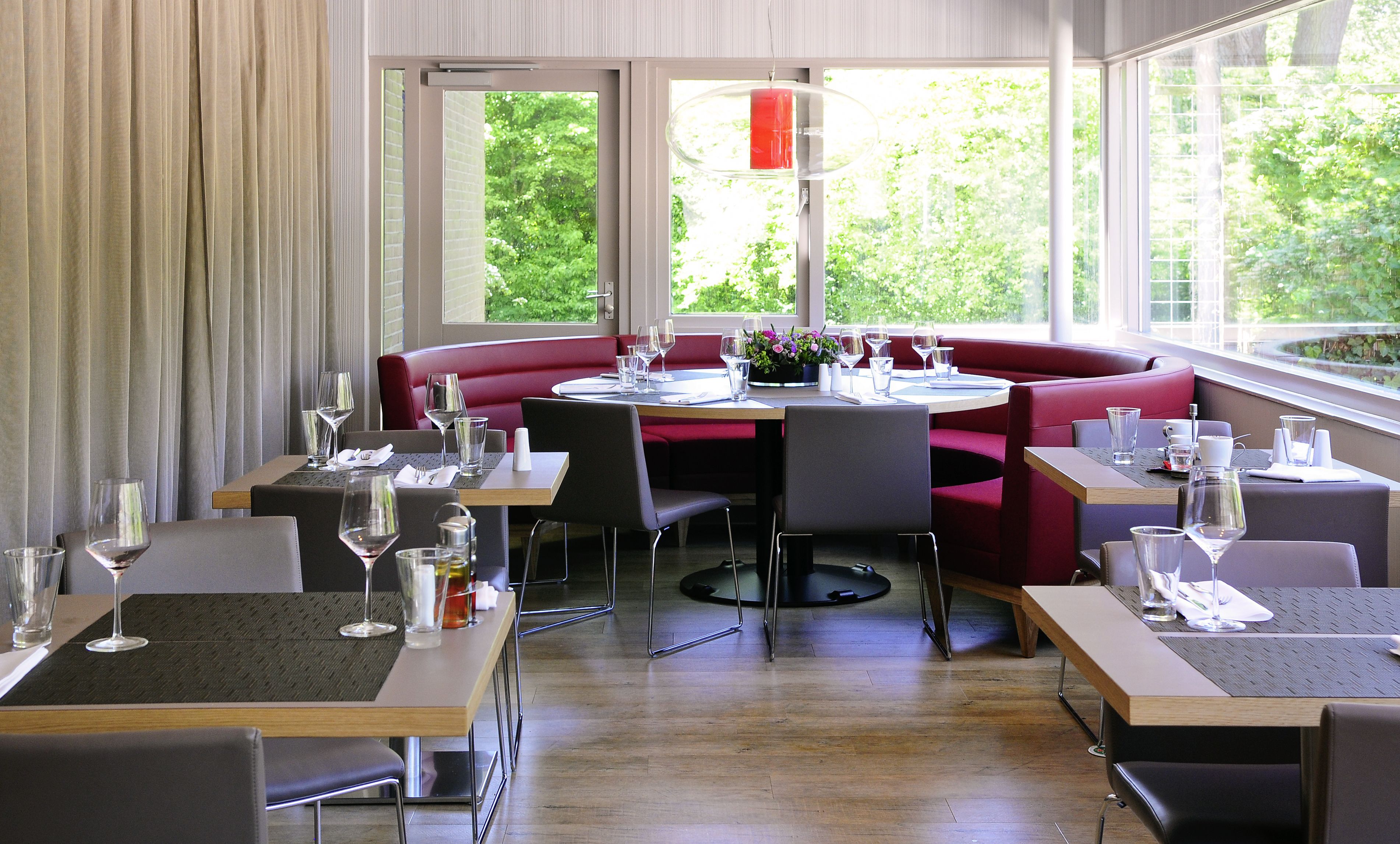 A restaurant with a modern interior, featuring red booths and wooden tables.