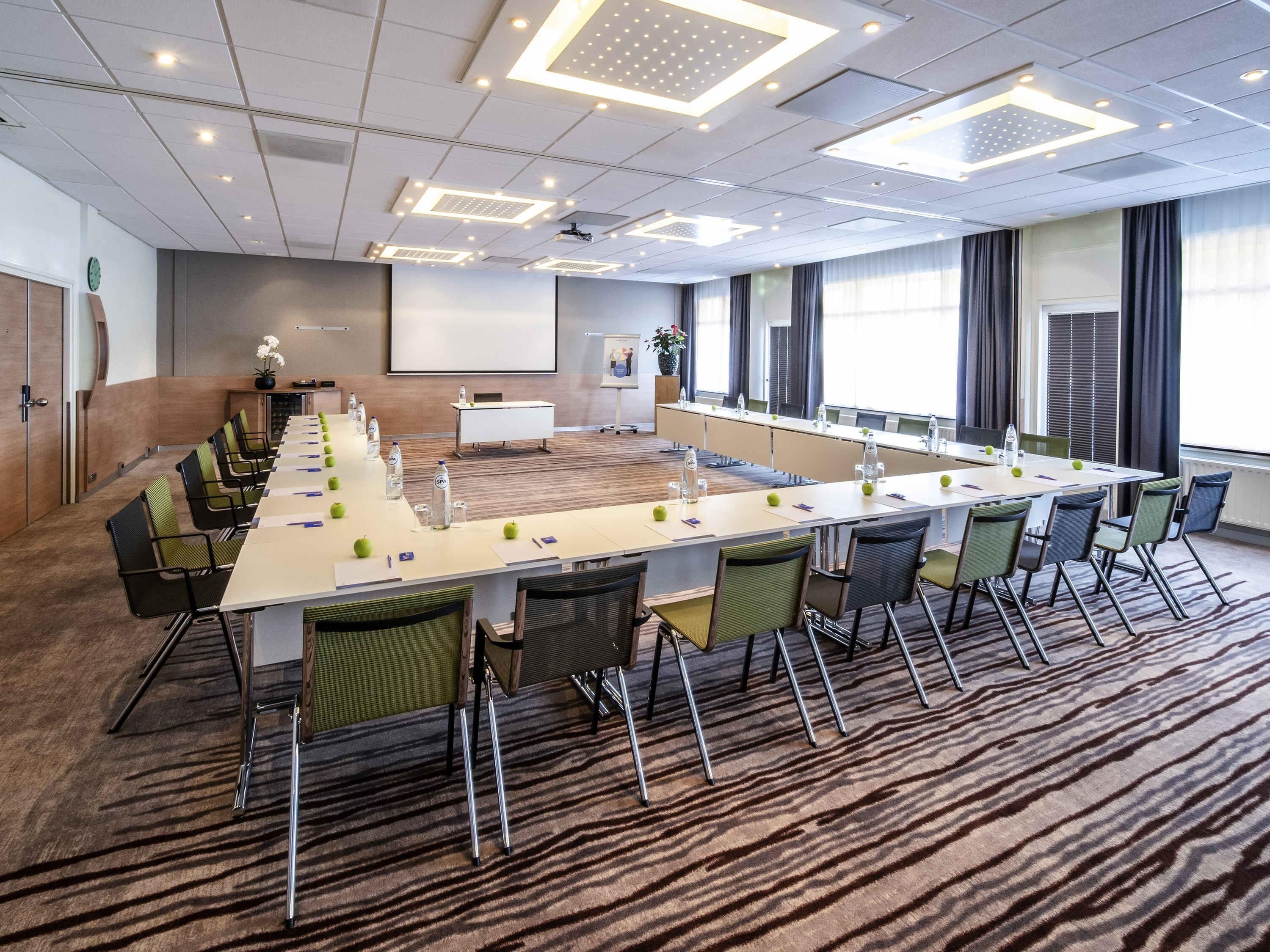 A conference room with a long table, chairs, a projector screen, and a presentation board.