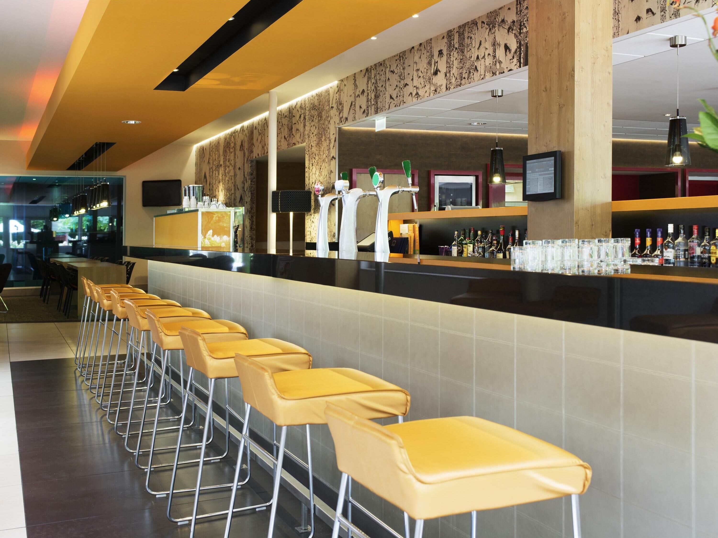 A bar area with a long counter, multiple stools, and a bar stocked with bottles.