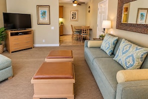 A living room with a television, a sofa, a coffee table, and a dining area with chairs and a table.
