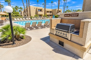 An outdoor pool area with lounge chairs, a grill area, and a clear sky.