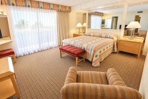 A hotel room with a bed, a bench, a chair, a desk, a mirror, and a window with curtains.