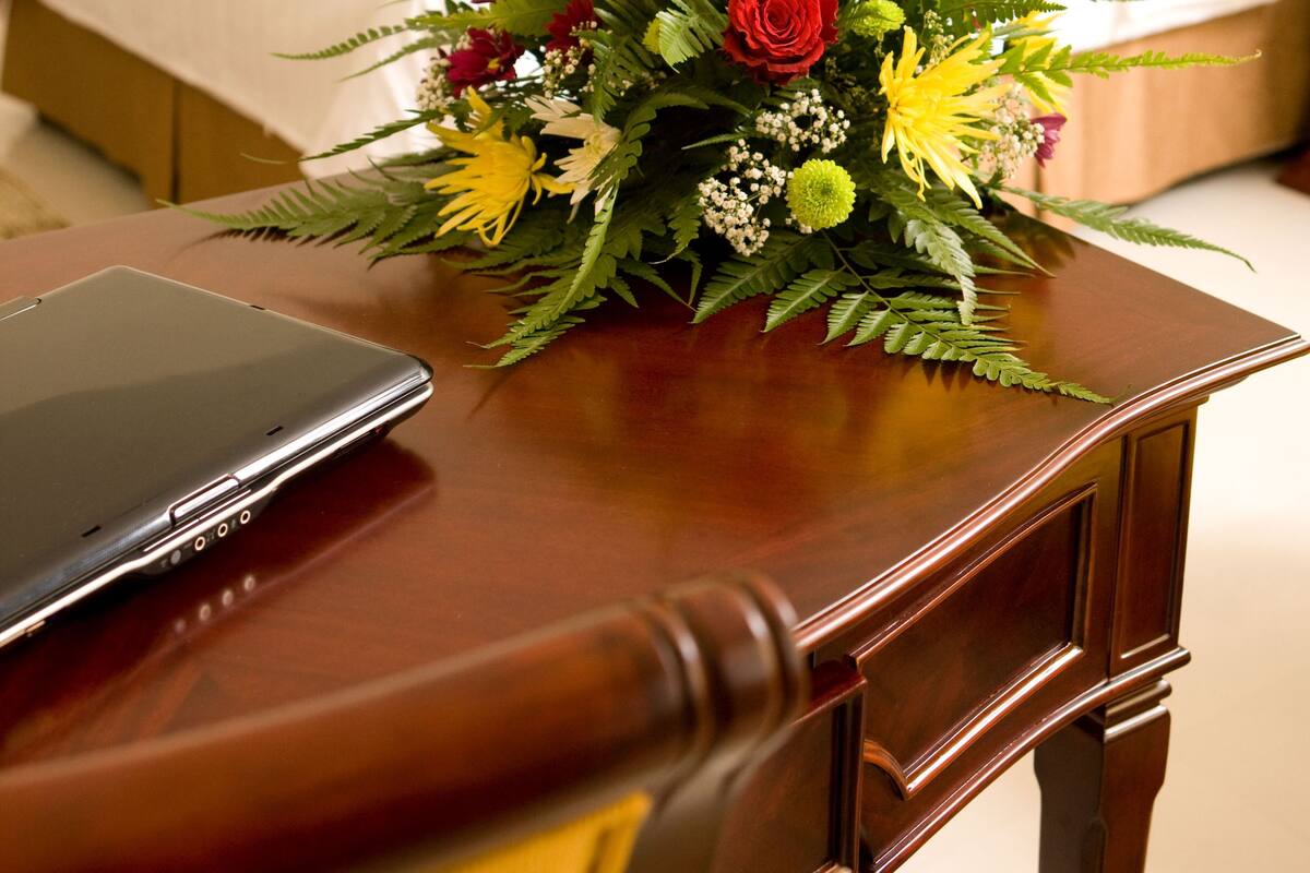 En snyggt bäddad säng med en sänggavel i trä, ett nattduksbord med en smartphone och en blomsteruppsättning på bordet.