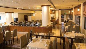 A restaurant with multiple dining tables, a central bar area, and a staircase leading to an upper level. - Hotel Muscat Holiday (Muscat)