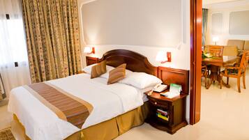 Habitación de hotel con una cama grande, mesitas de noche con lámparas, un escritorio con una silla y vista al interior de la habitación.