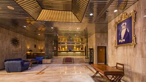 A lobby with a marble floor, a reception desk, sofas, a dining table, and a framed portrait on the wall. - Hotel Muscat Holiday (Muscat)