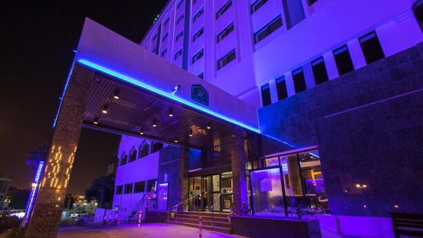 A hotel entrance with a modern design, featuring a covered entrance area and a visible parking sign. - Hotel Muscat Holiday (Muscat)