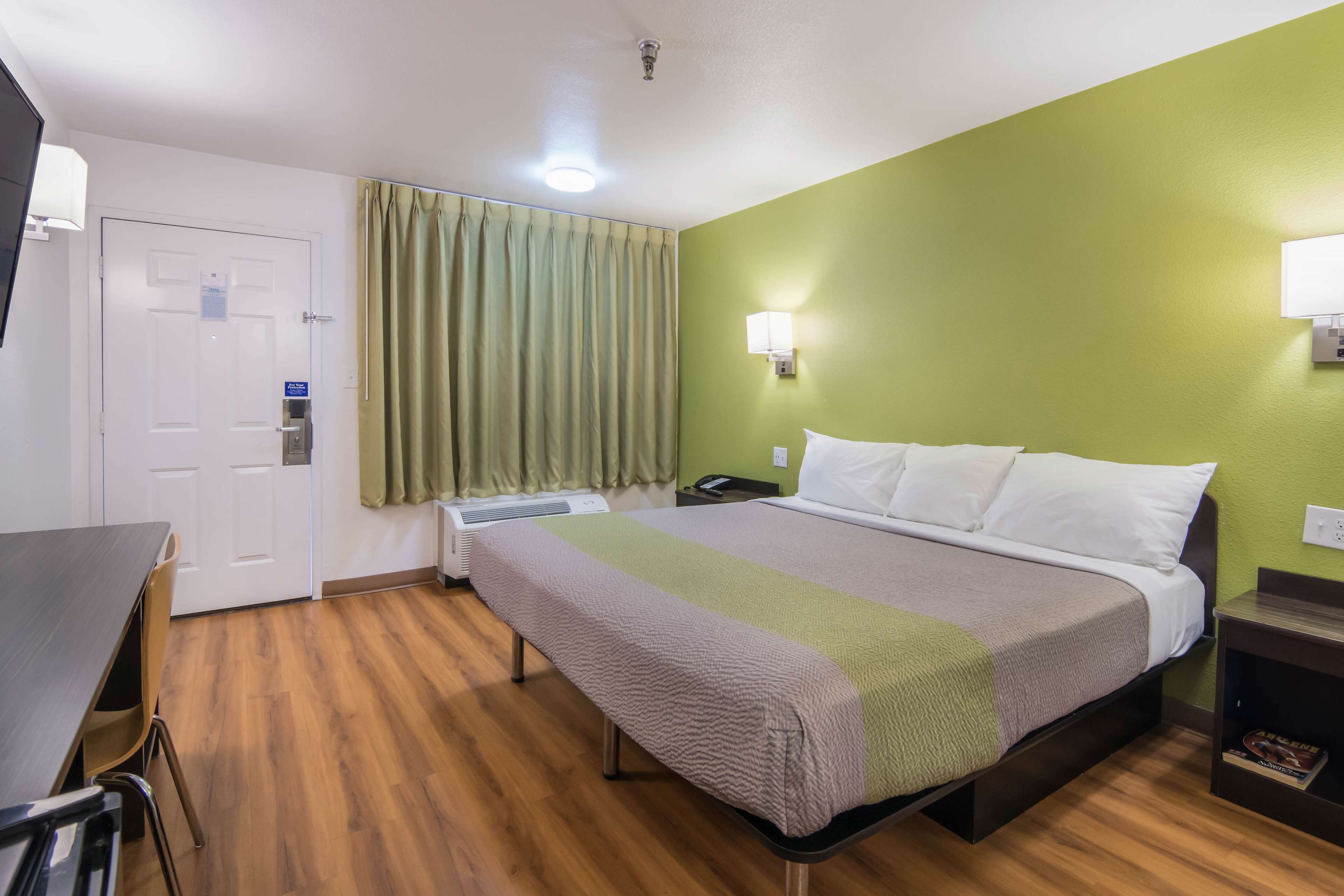 A hotel room with a bed, a desk, a chair, a door, and a window with curtains.