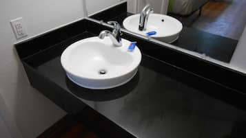 Une salle de bain avec un lavabo blanc, un plan de toilette noir et un miroir.