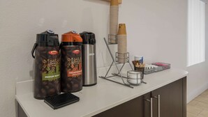 Una estación de café con dos dispensadores, un molinillo y una pila de vasos desechables.