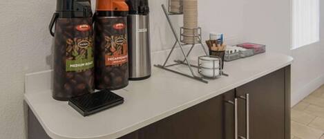 A coffee station with two coffee dispensers, a scale, and a stack of disposable cups.